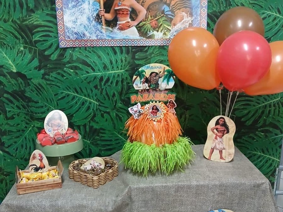 Mesa do tema Ilha tropical na Comemorando Festas, com painel, folhagens, bexigas e topo de bolo