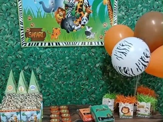 Mesa do tema Safári na Comemorando Festas, com painel de animais, bexigas laranja e marrom e lembrancinhas